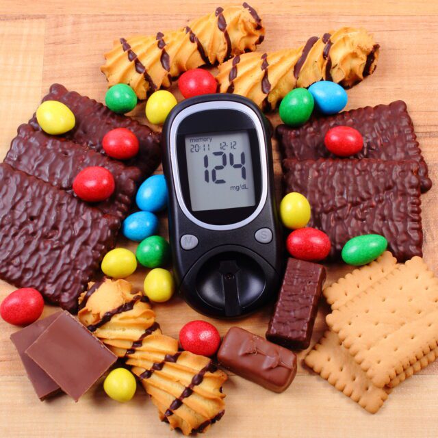 Glucometer with heap of sweets on wooden surface, diabetes and u