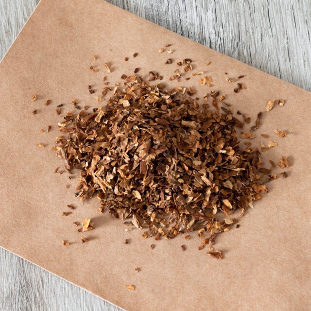 A square photo of dried sliced tobacco or a smoking drug mixture. Smoking drugs on paper close-up on a wooden table.