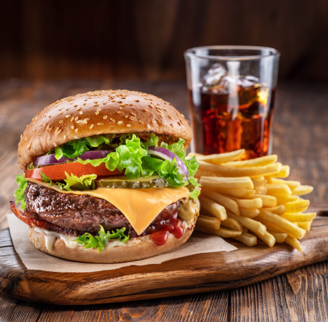 Delicious hamburger with cola and potato fries on a wooden table with a dark brown background behind. Fast food concept.