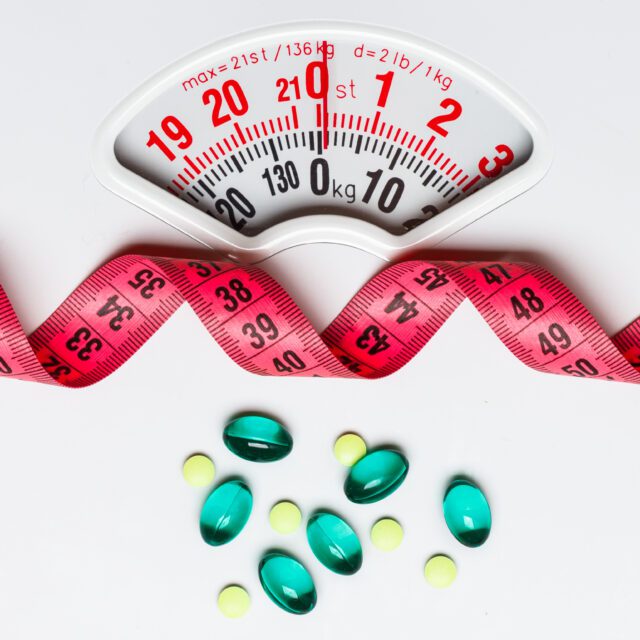 Pills with measuring tape on white scales